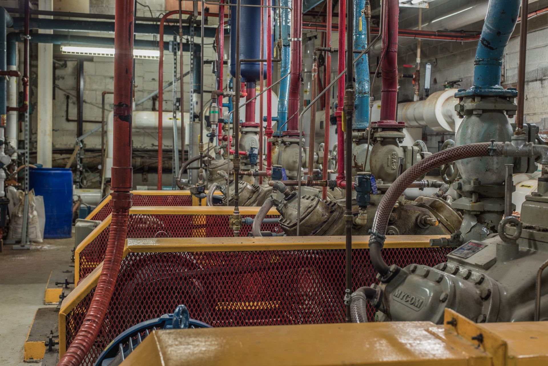 Industrial machinery with red, blue, and yellow pipes, and metal barriers in a dim room.