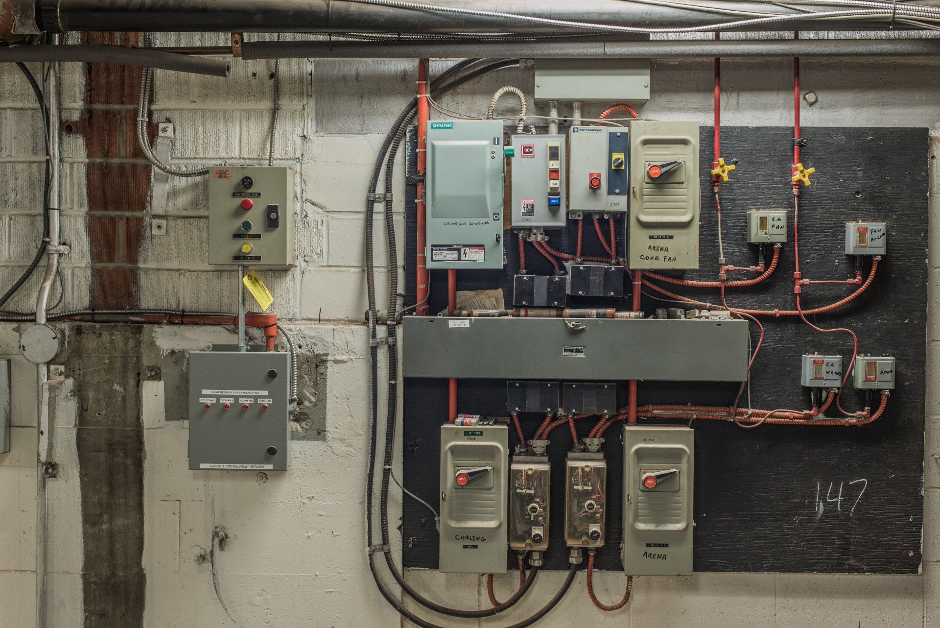 Electrical panel on a concrete wall with various switches, wires, and boxes.