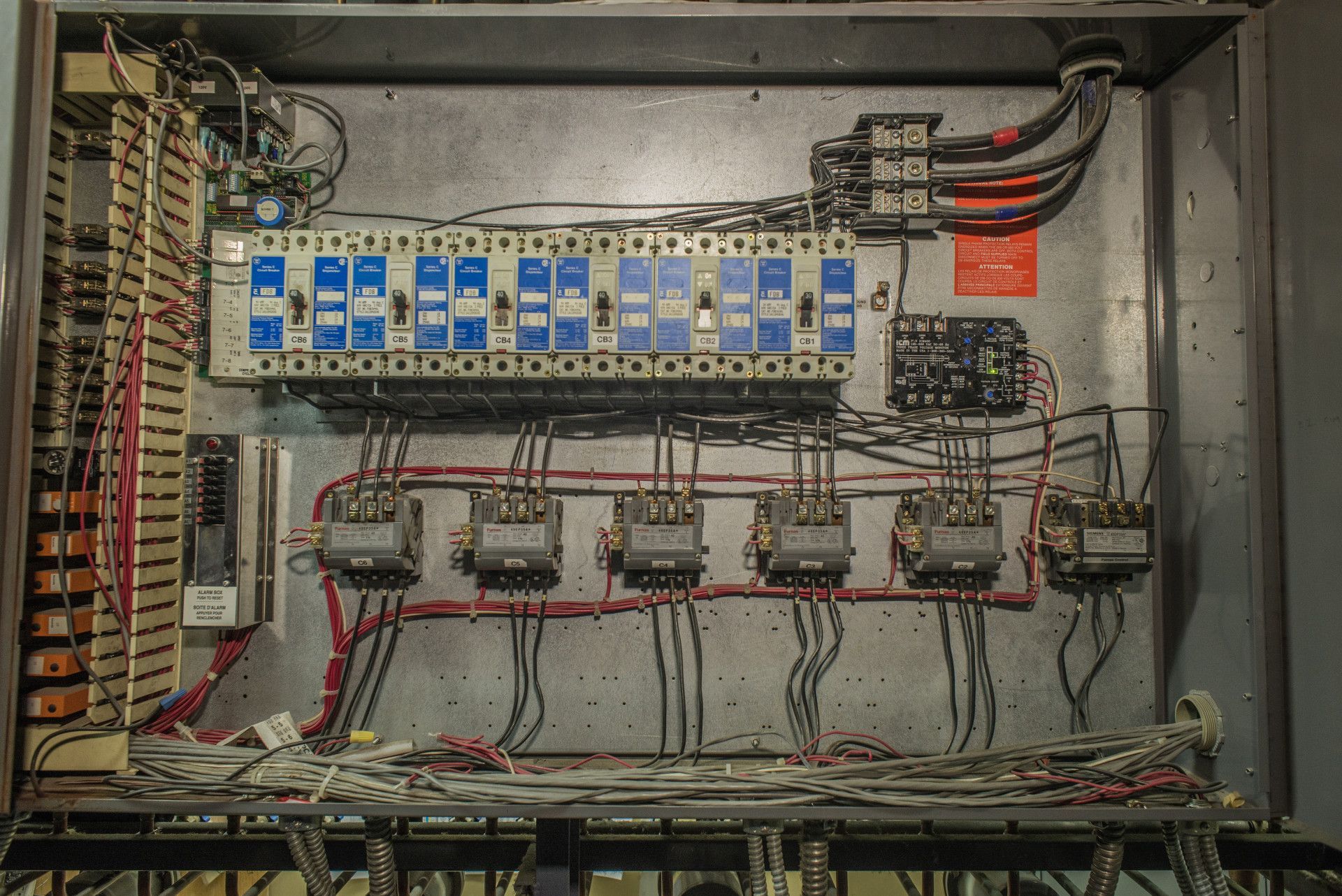 Electrical control panel with wiring, fuses, and relays inside a metal enclosure.