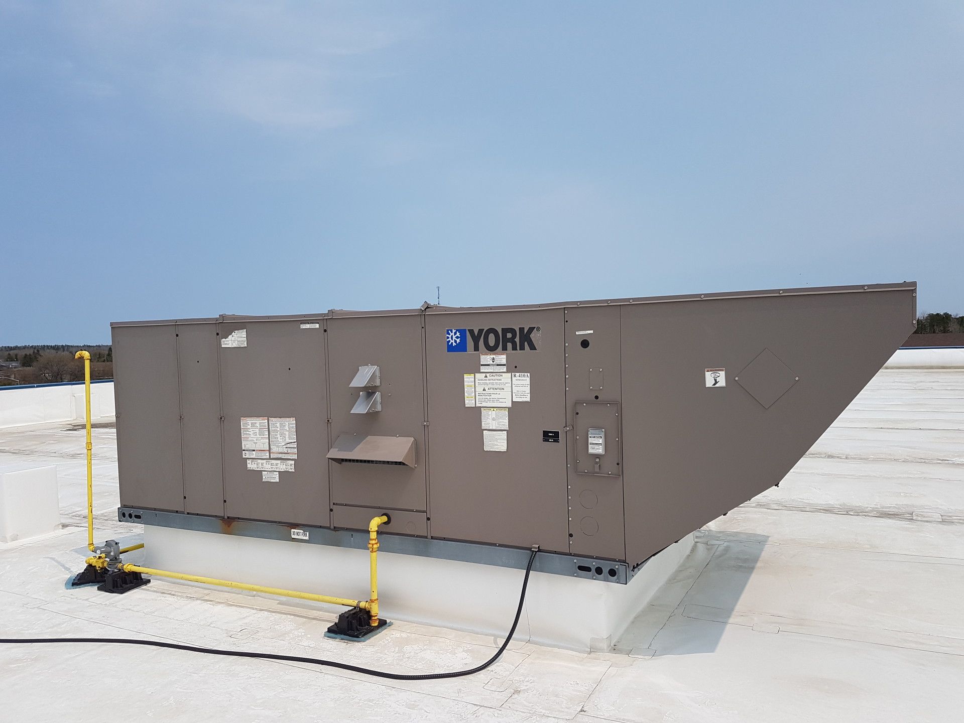 A rooftop HVAC unit by York on a white roof under a blue sky.