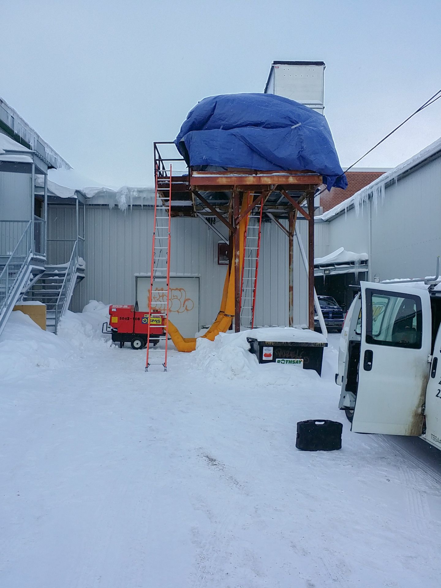 Snowy outdoor scene with a structure covered in blue tarp and construction equipment.