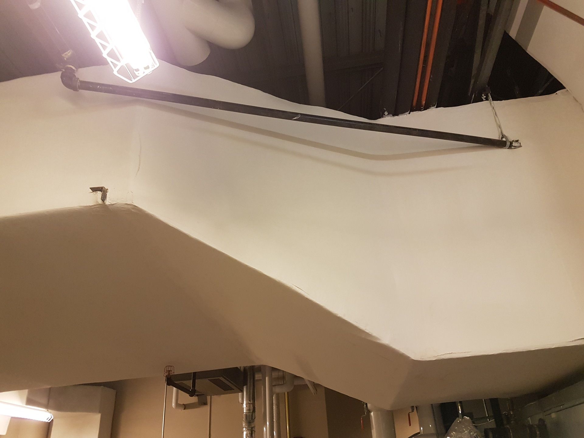 Black pipe suspended from ceiling, running diagonally across white walls.