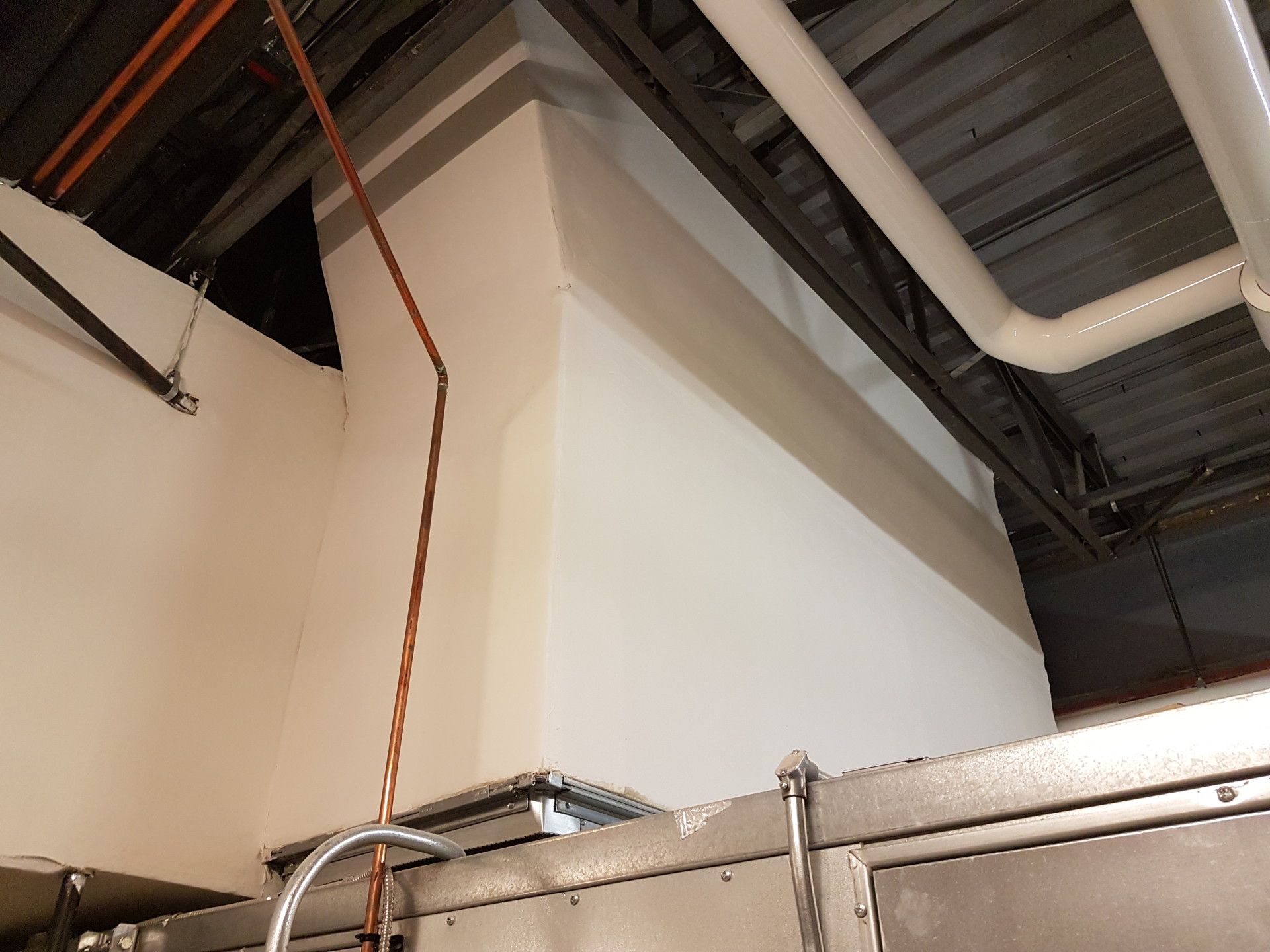 White wall with copper pipe, above a metal machine in a commercial setting.