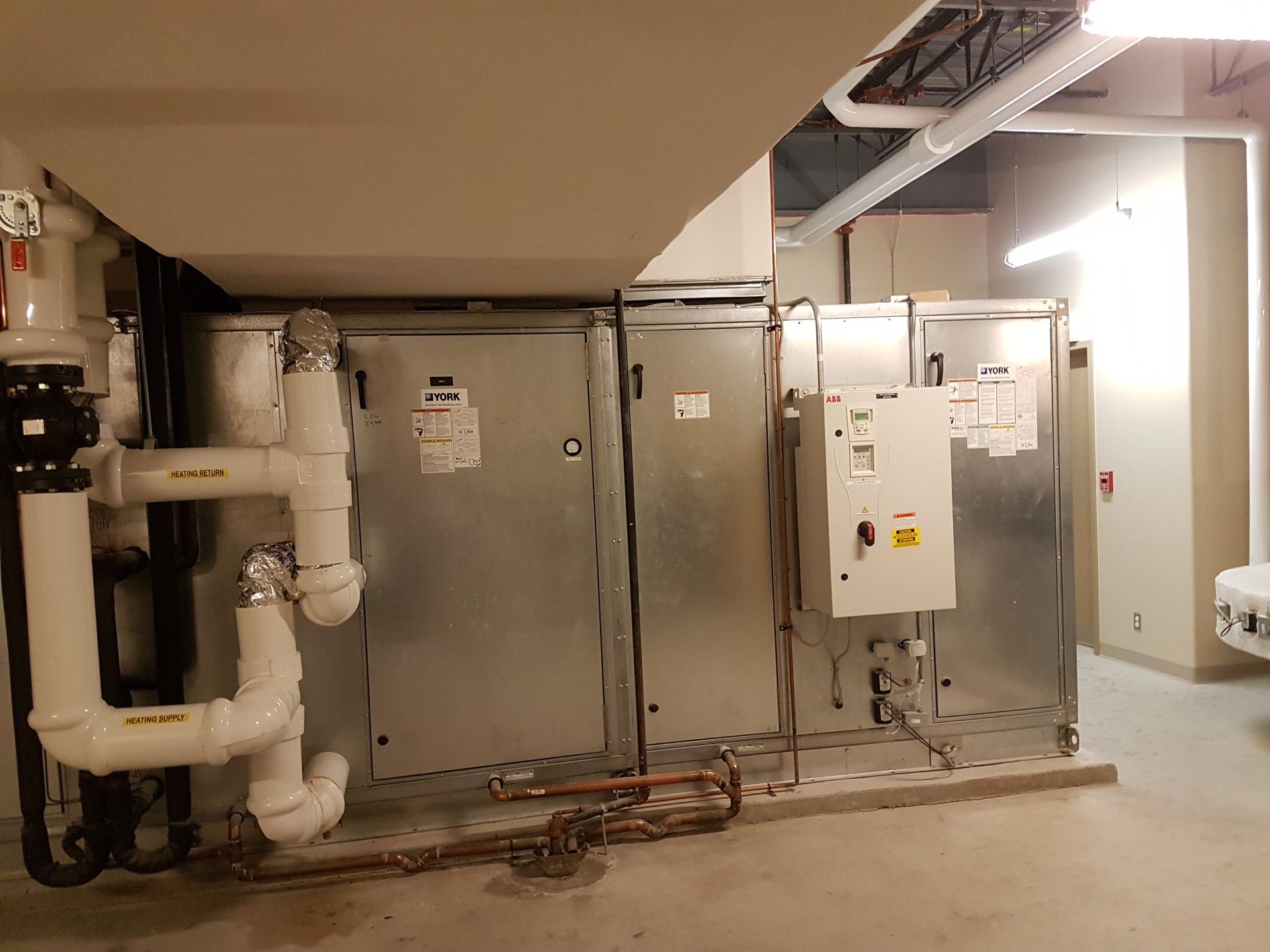 Large, metal HVAC unit in a room, with white pipes and electrical components.
