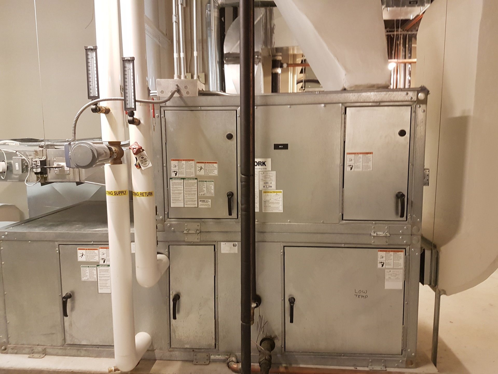 Large, gray HVAC unit with various panels and ductwork in a utility room.