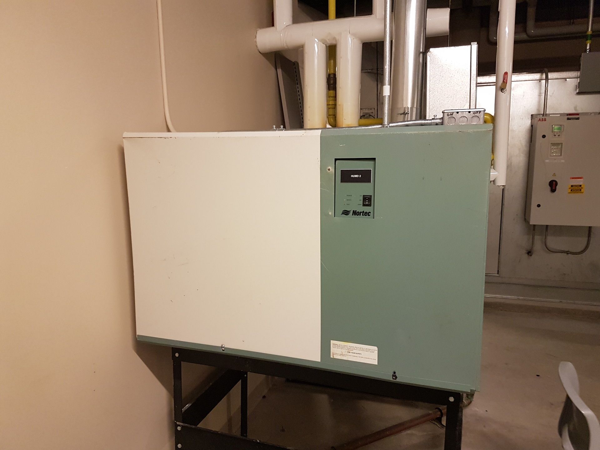 Green and white industrial heater on a black metal stand, in a basement.