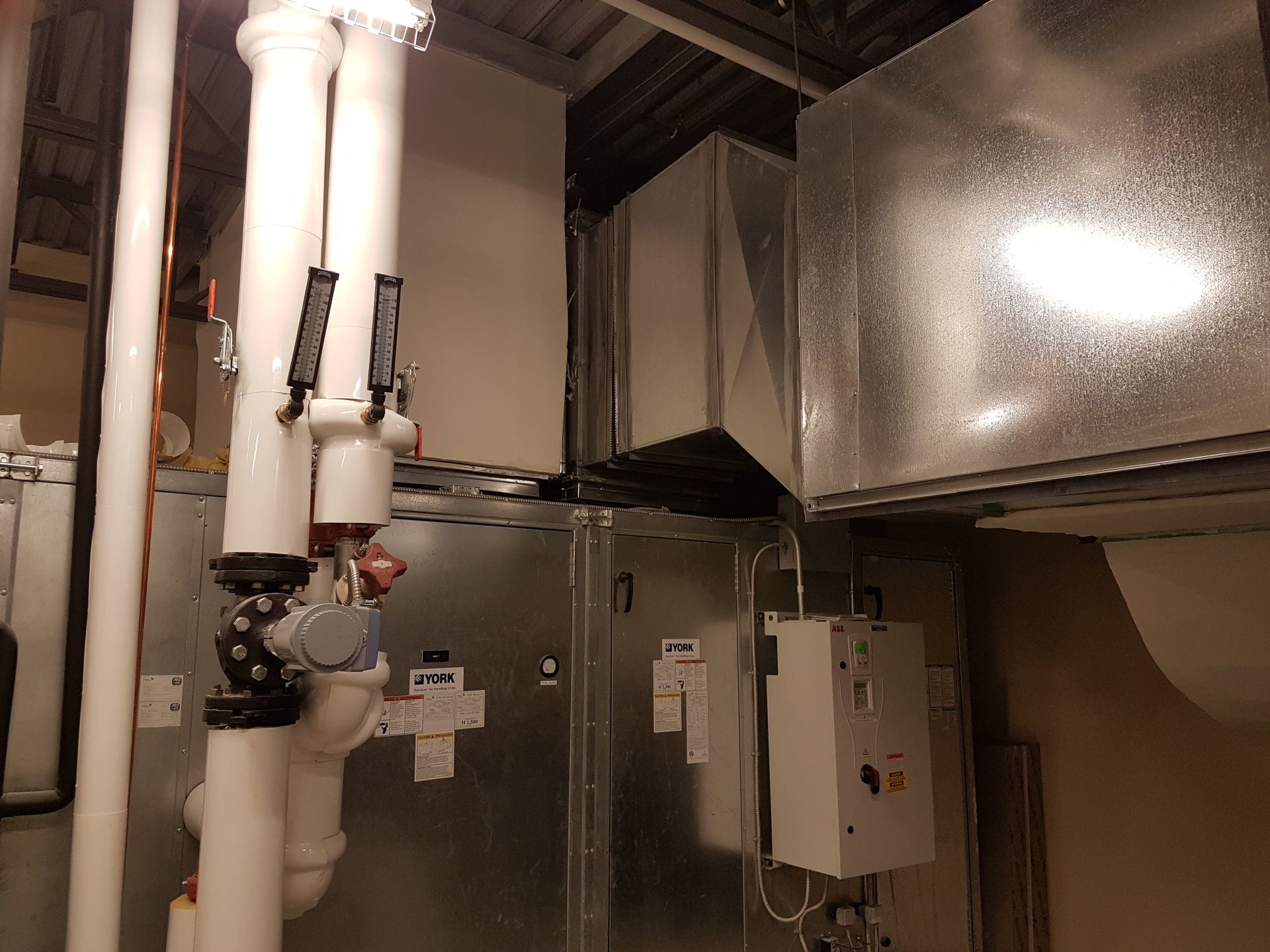 HVAC system with insulated white pipes, metallic ductwork, and control panel in an industrial setting.