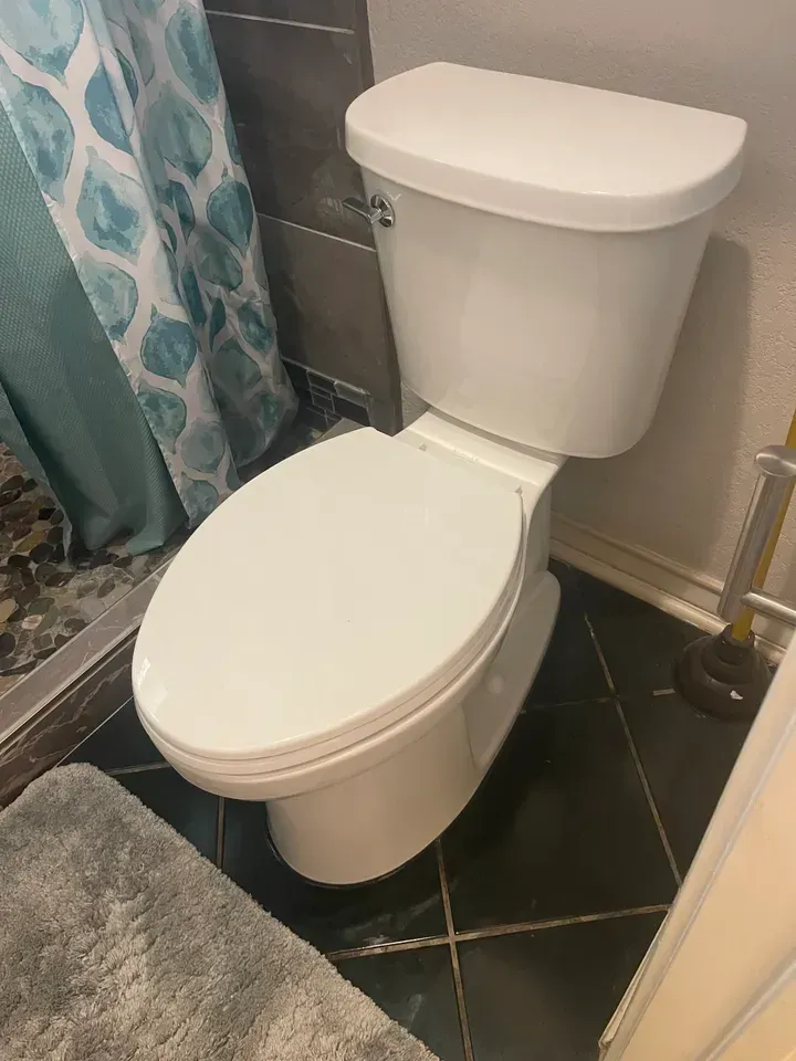 White toilet in a bathroom with a blue shower curtain and dark tiled floor.