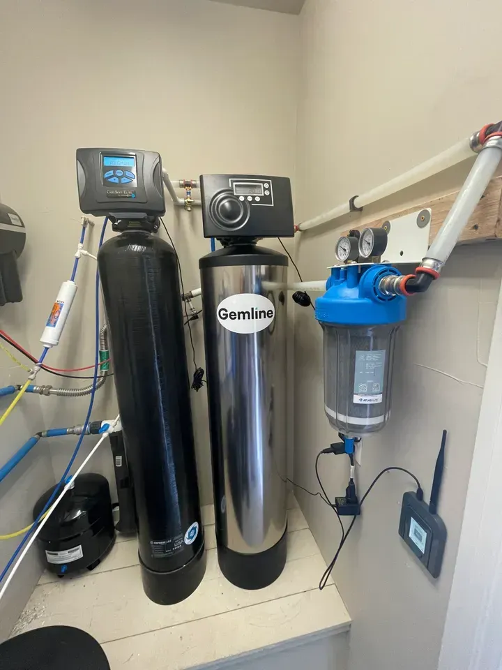 Water filtration system with three tanks: black, stainless steel, and blue, mounted in a utility room.