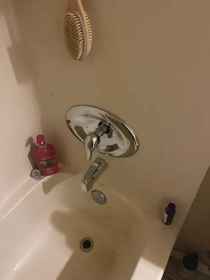 A bathtub with chrome faucet and showerhead, with toiletries and a brush hanging above.