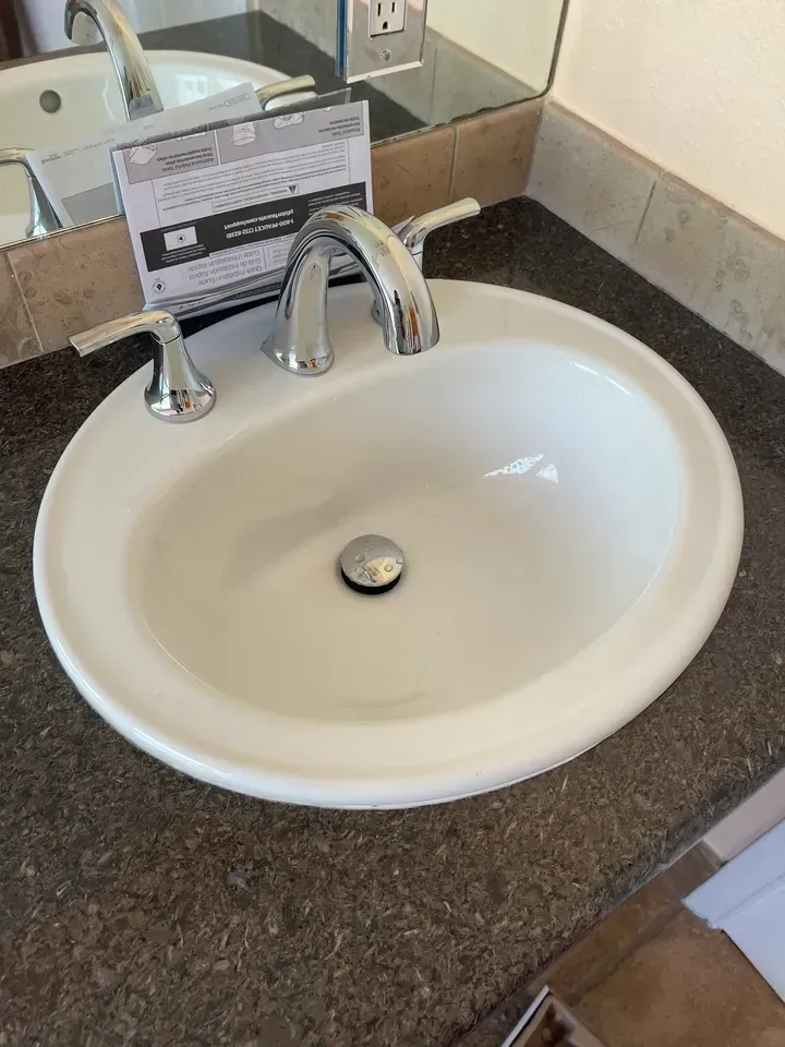 White oval bathroom sink with chrome faucet and handles on dark speckled countertop.