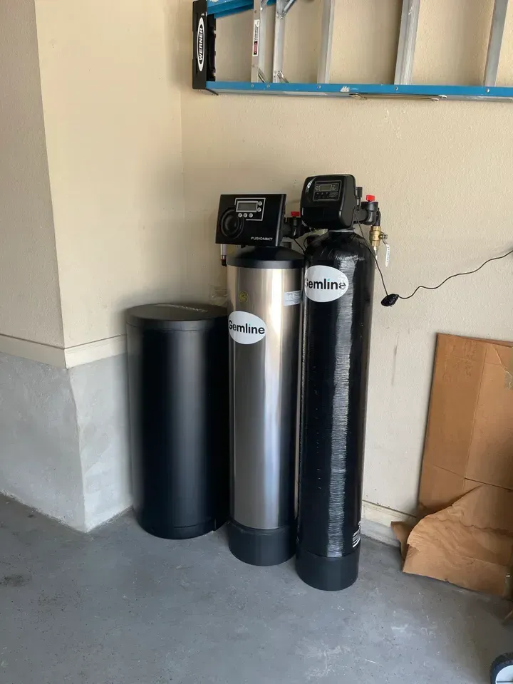 Water filtration system in a garage: three tanks, one black and two silver, against a beige wall.