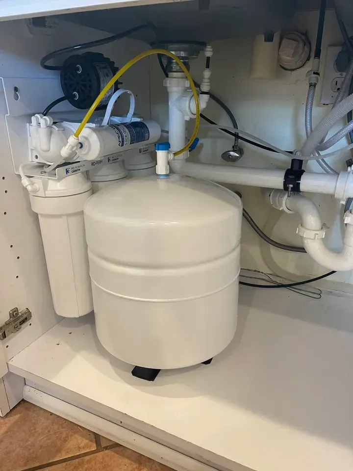 Under-sink water filtration system with a white tank, filters, and plumbing.