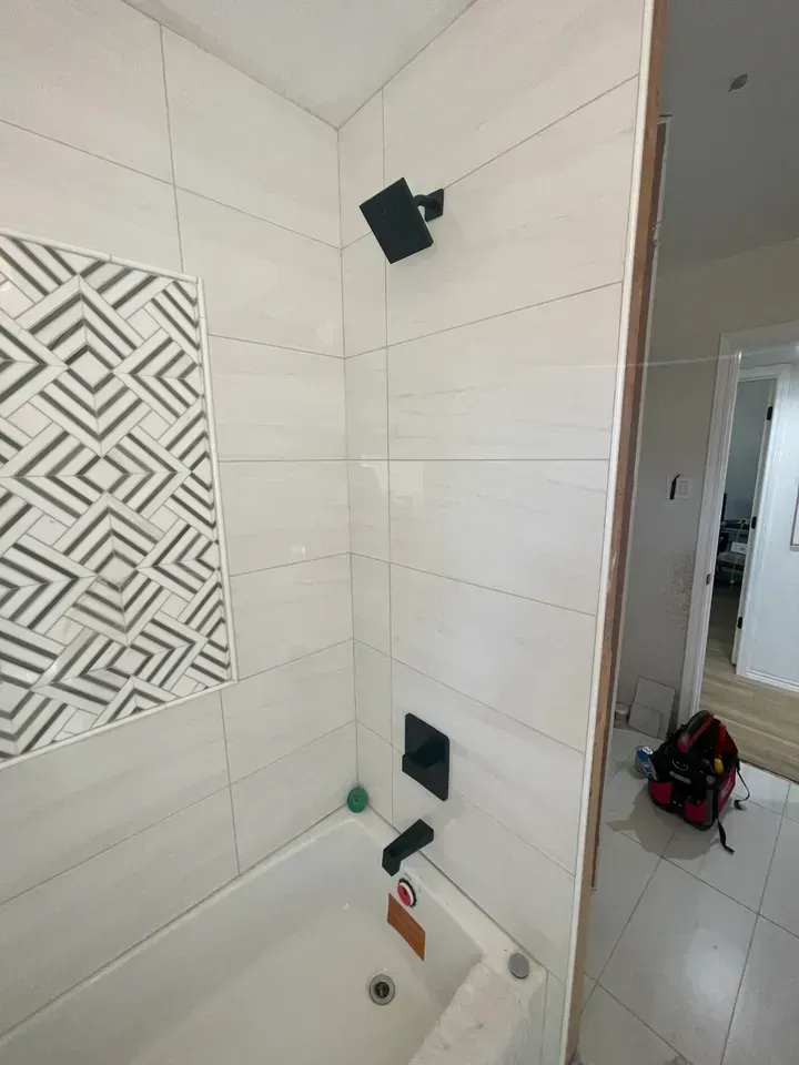 Modern shower with white and patterned tiles, black fixtures, and a bathtub.