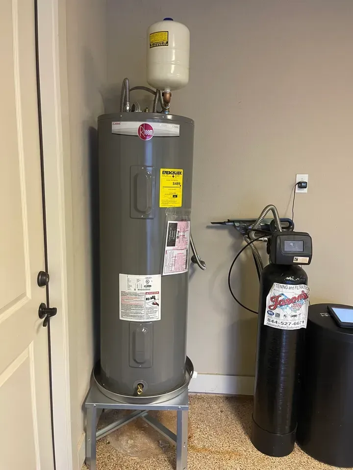 Water heater and water softener in a garage. Gray water heater with white expansion tank, next to a black softener.