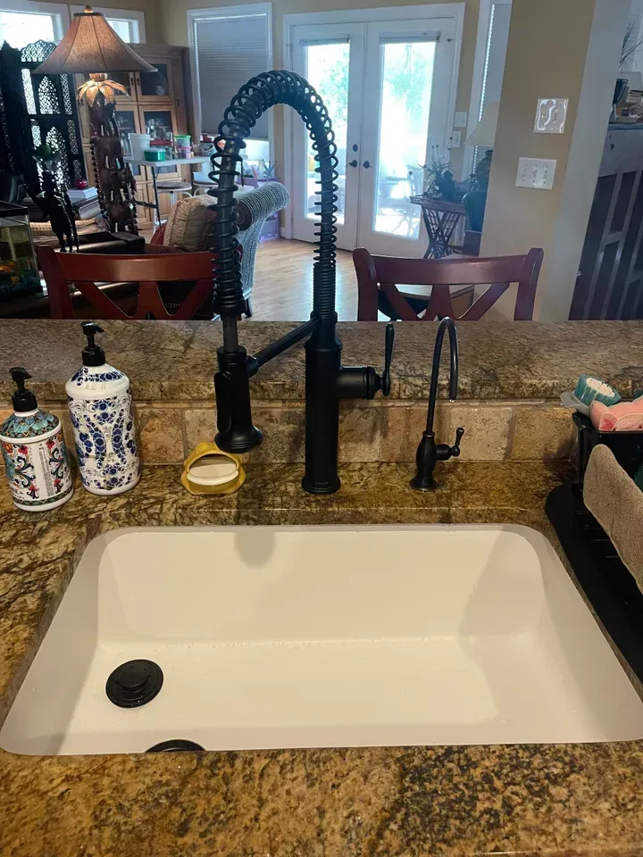 Black kitchen faucet over a white sink, two soap dispensers, set on a granite countertop.