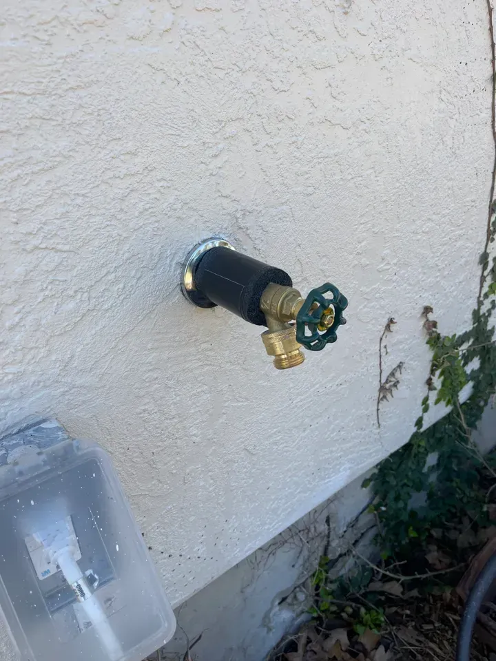 Outdoor spigot attached to a stucco wall, with a green handle and black insulation.