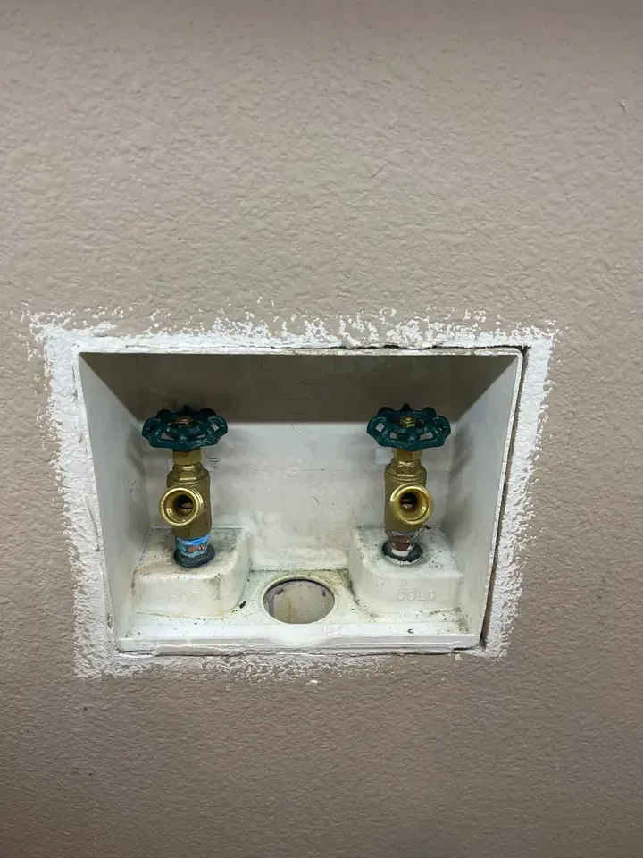 White recessed box with two brass water shut-off valves. A hole for a drain is in the middle.