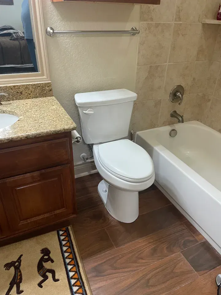 Bathroom with toilet, bathtub, vanity, and wood-look flooring. Beige tile on walls.