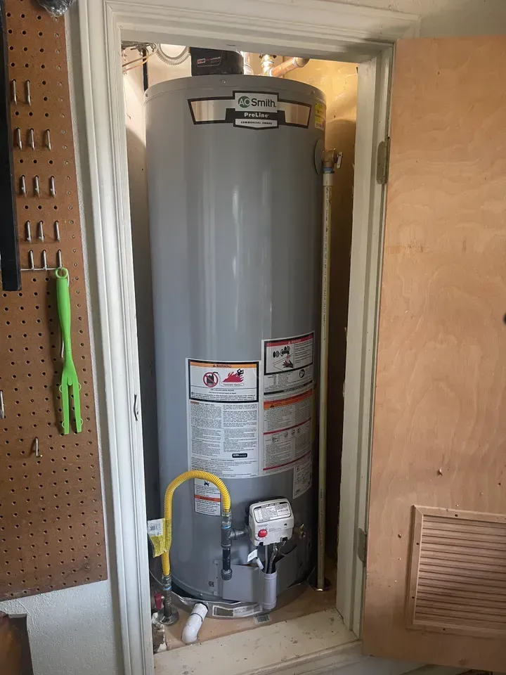 A tall, gray water heater inside a small, wooden closet. A yellow gas line is visible.