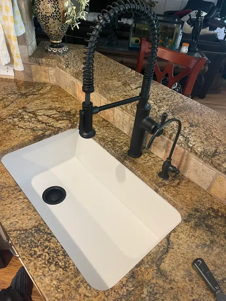 White kitchen sink with black faucet on a speckled countertop.