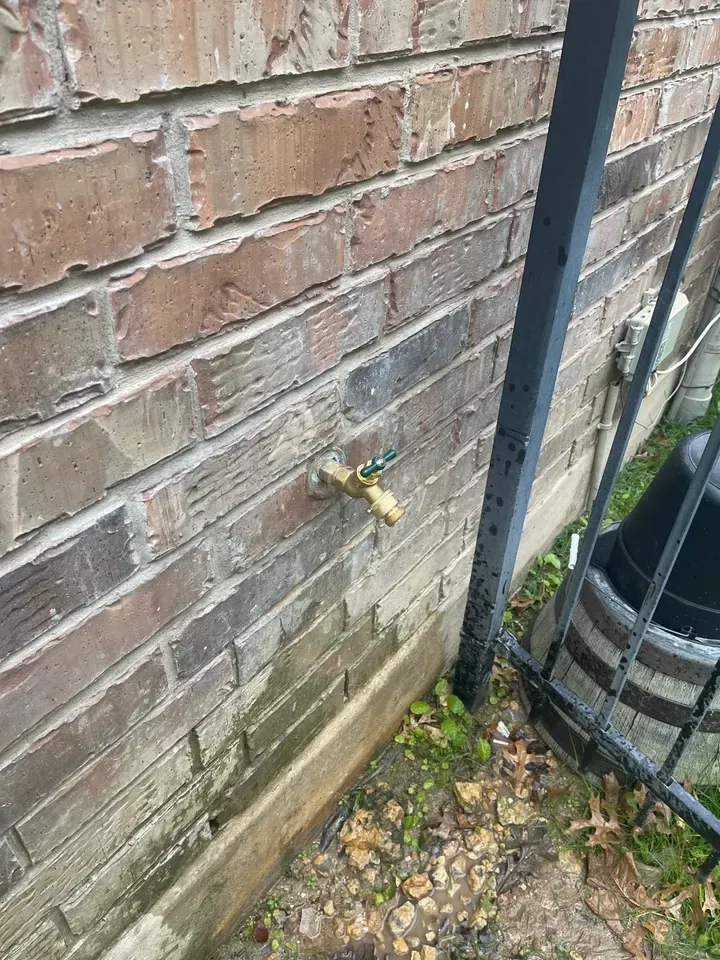 Brick wall with outdoor faucet. A black gate and barrel are to the right.