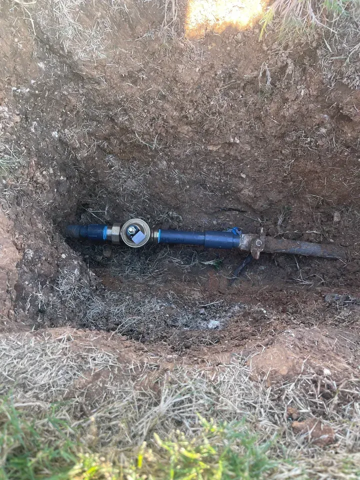 Blue water pipe with valve exposed in a dirt trench.
