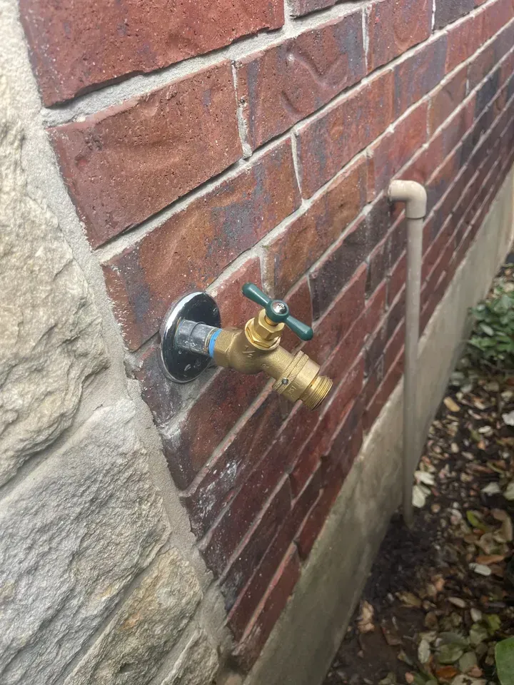 Brass water faucet with green handle mounted on a red brick wall.