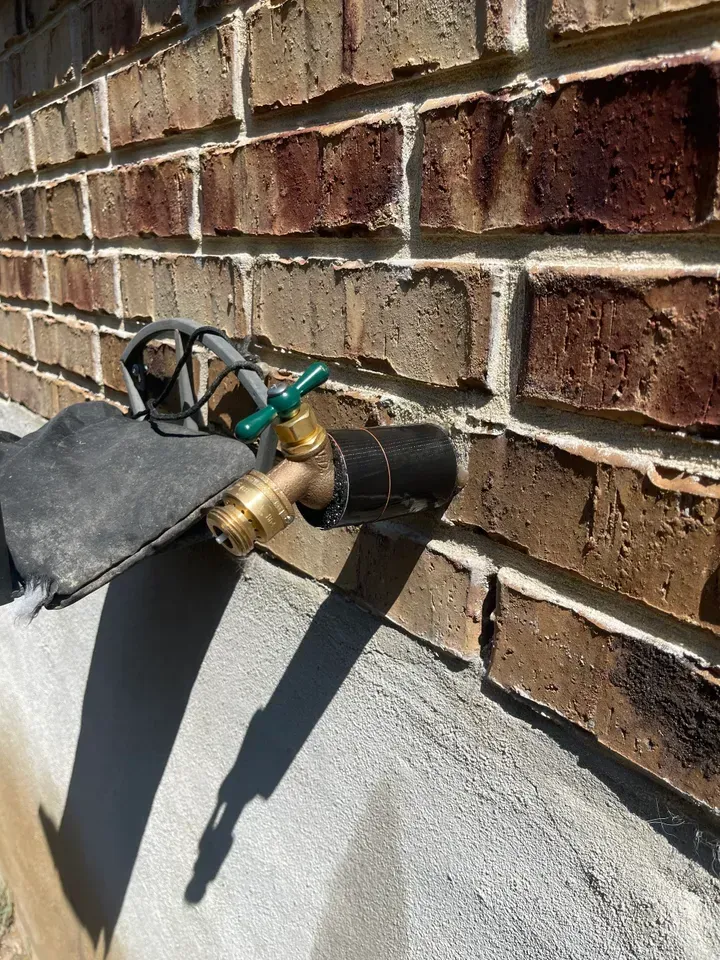 A brick wall with a brass faucet and black insulation. Green handle, concrete base.