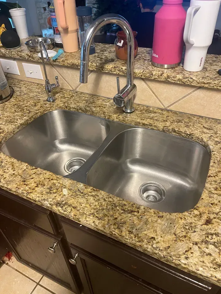 Stainless steel double sink with faucet on a granite countertop.