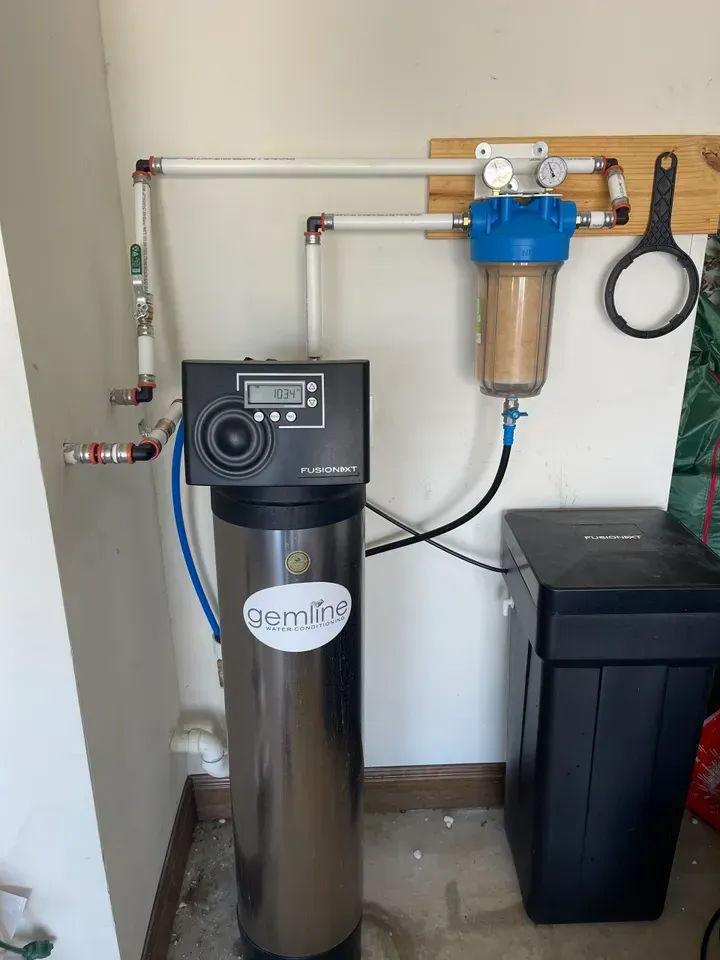 Water filtration system in a garage;  a tall silver tank, a blue filter, and a black salt tank.