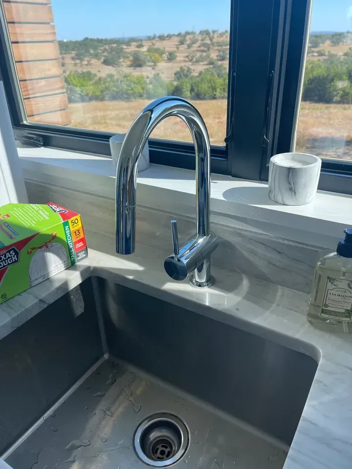 Kitchen sink with chrome faucet in front of a window overlooking a landscape.