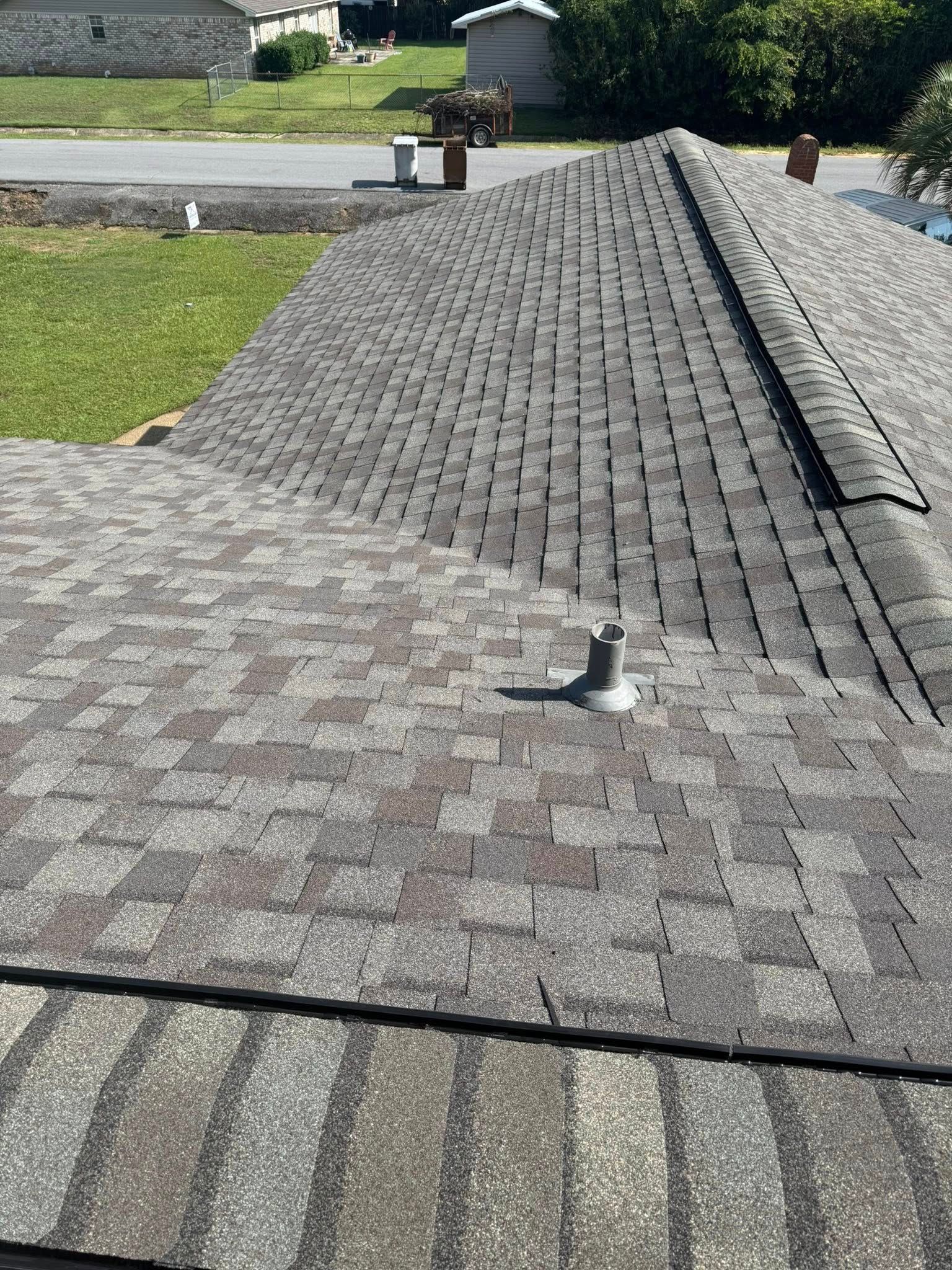 Close-up of a house roof with asphalt shingles. Gray and brown shingles cover the roof with vents and chimneys.