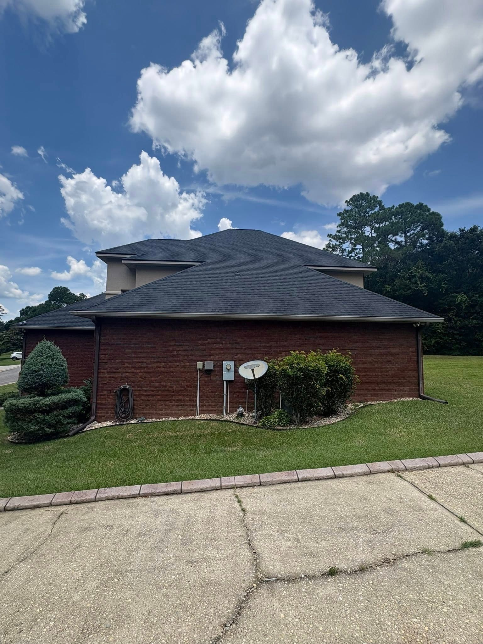 Brick house with dark roof and antenna under a partly cloudy sky.