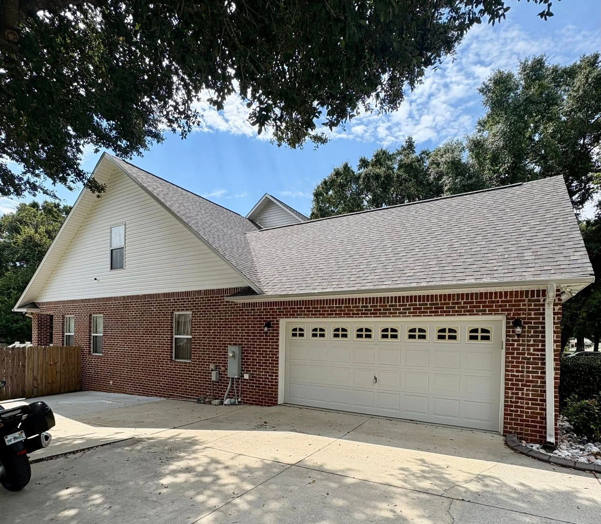 Brick house with a white garage door, asphalt shingle roof, and a concrete driveway.