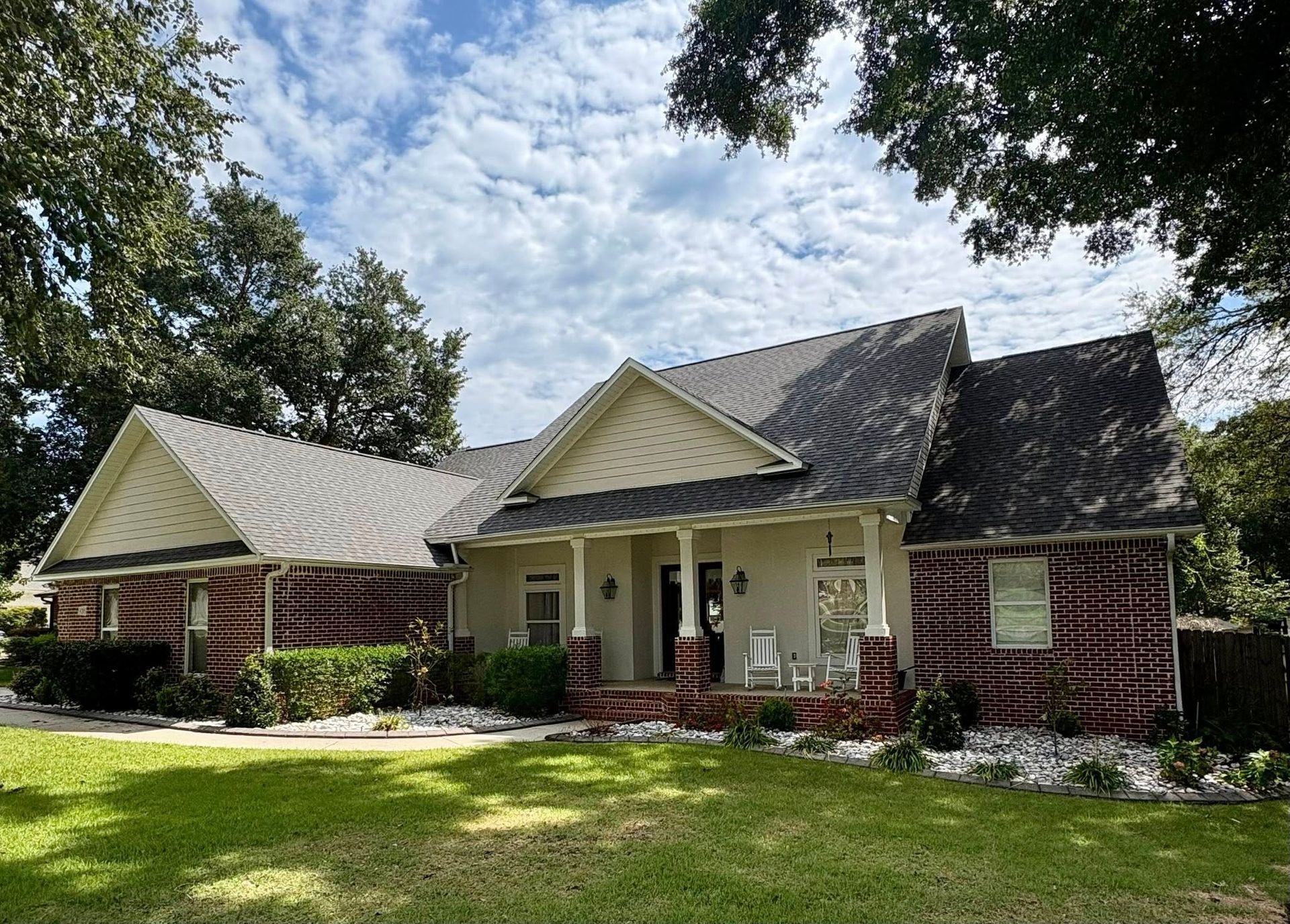 House with red brick and light siding, surrounded by greenery. Cloudy sky.