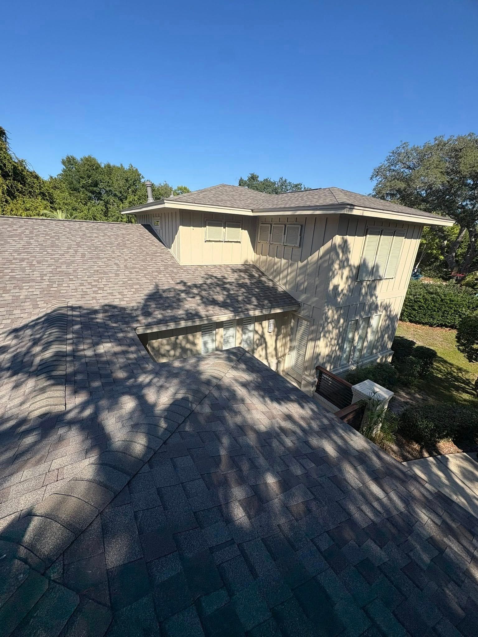 View of a house with a shingled roof, trees in the background, against a clear blue sky.