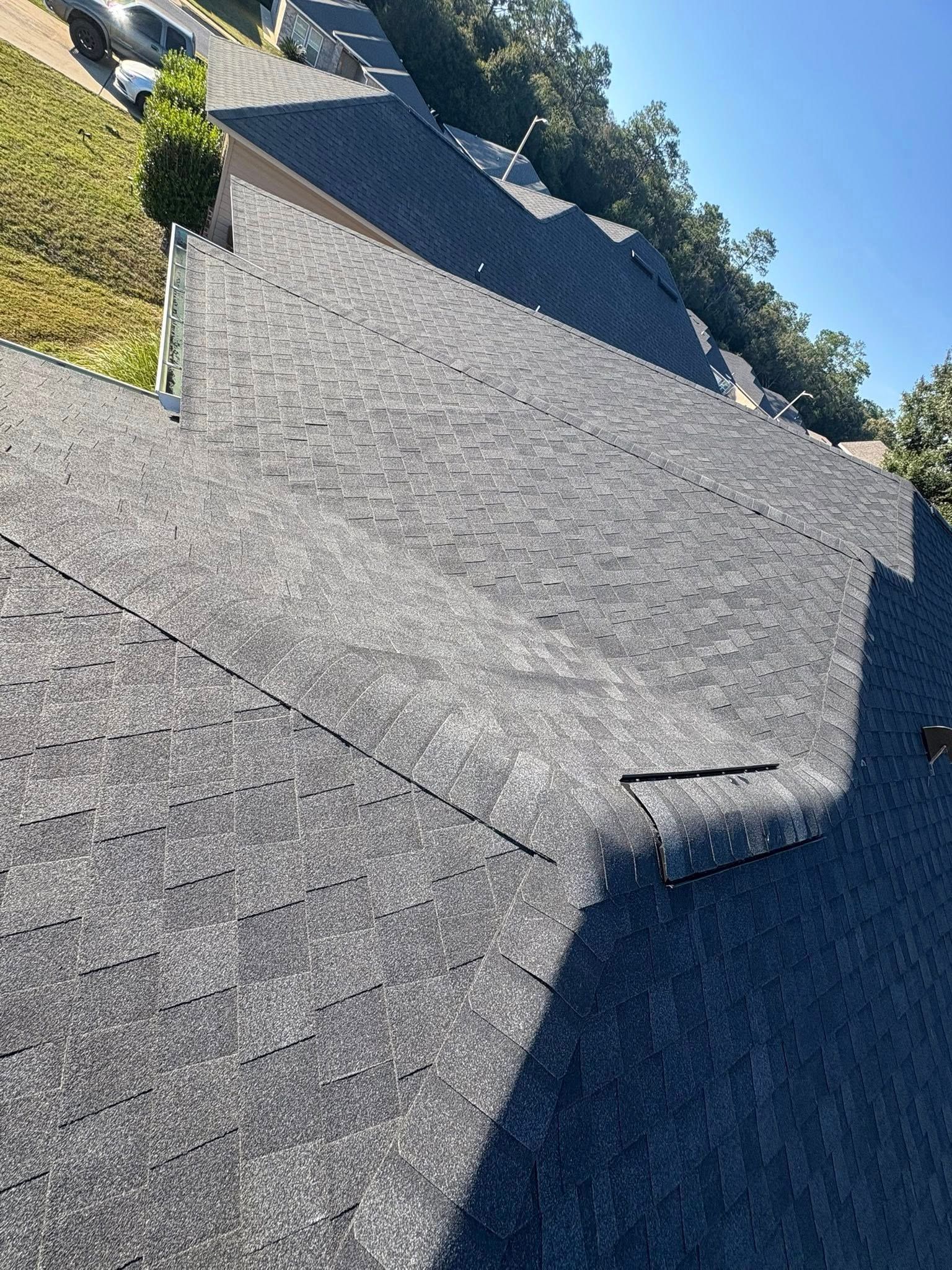 Gray asphalt shingle roof on a hillside residential building on a sunny day.