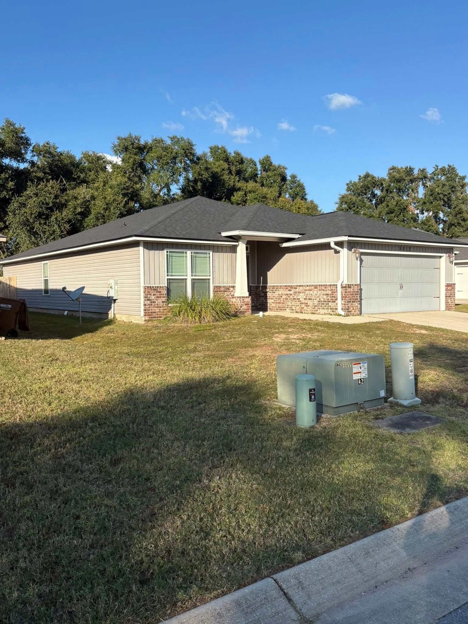 Single-story house with a gray roof and siding, brick facade, and a two-car garage under a blue sky.