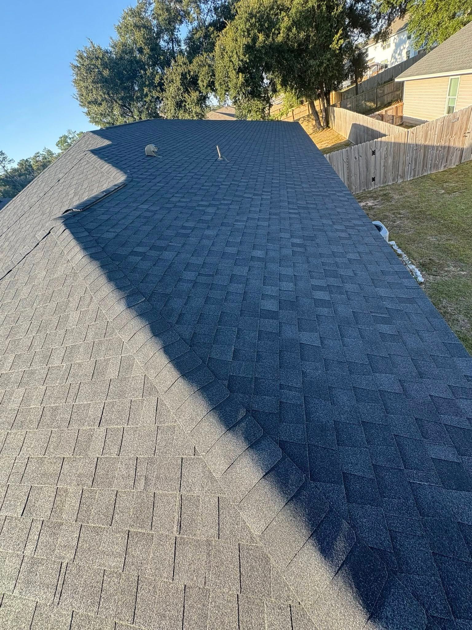 View of a dark gray asphalt shingle roof, with trees and a building in the background.