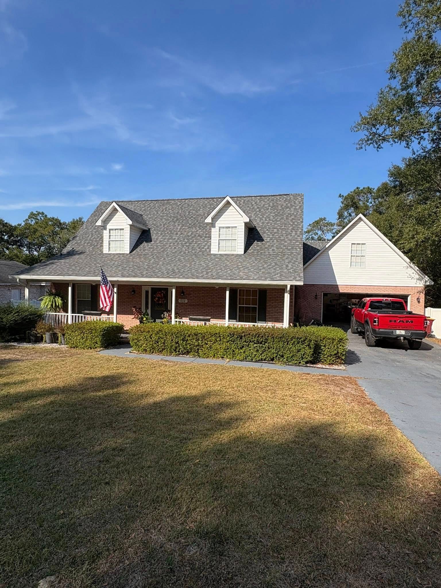 A two-story house with a brick facade and a gray roof, a red truck is parked in the driveway.