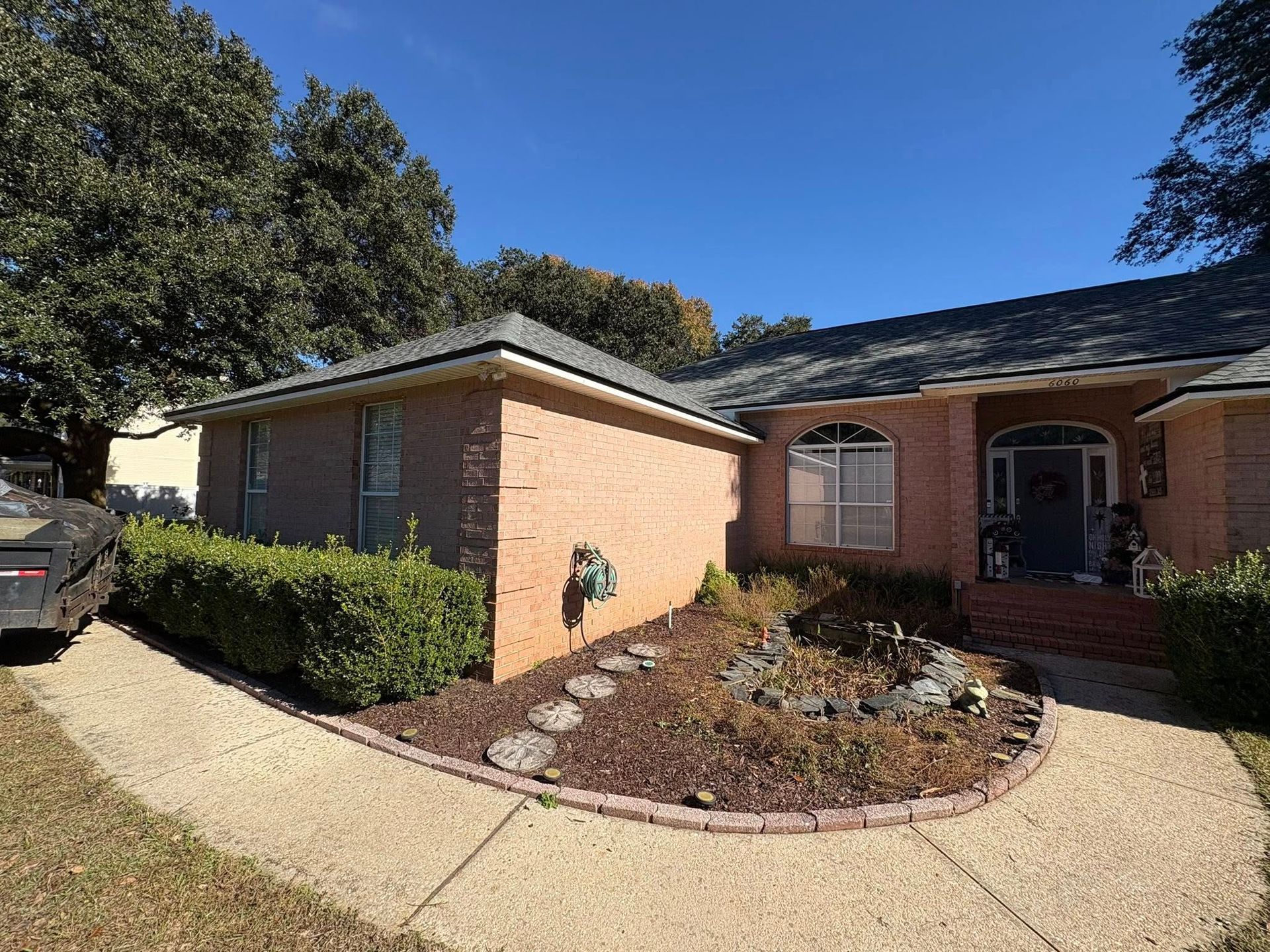Brick house with dark roof and landscaping, blue sky in the background.