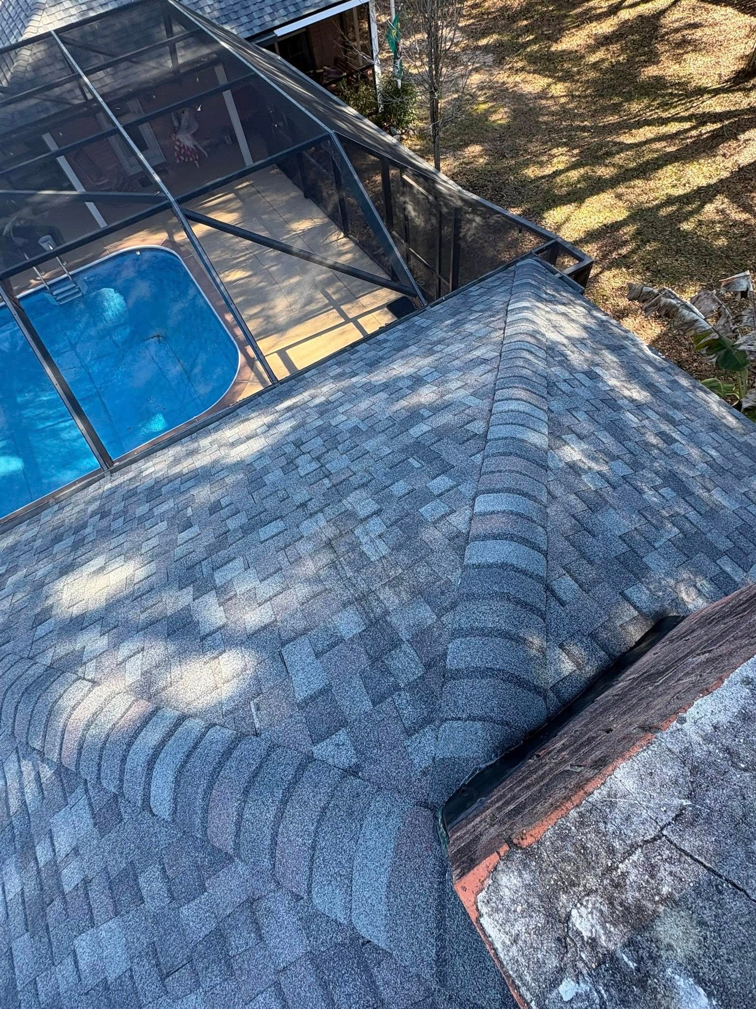 Overhead view of a gray shingled roof with a screened pool area in the background.