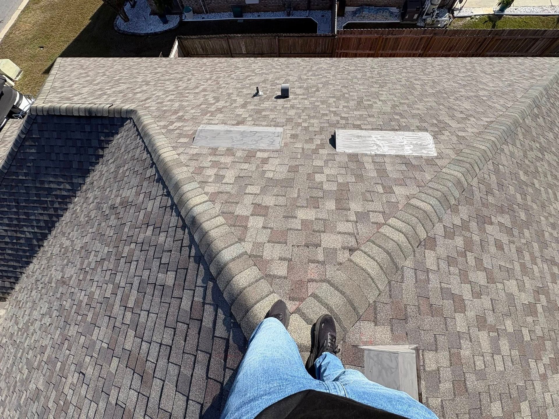 Person's legs and feet standing on a brown shingled roof with a shadow.