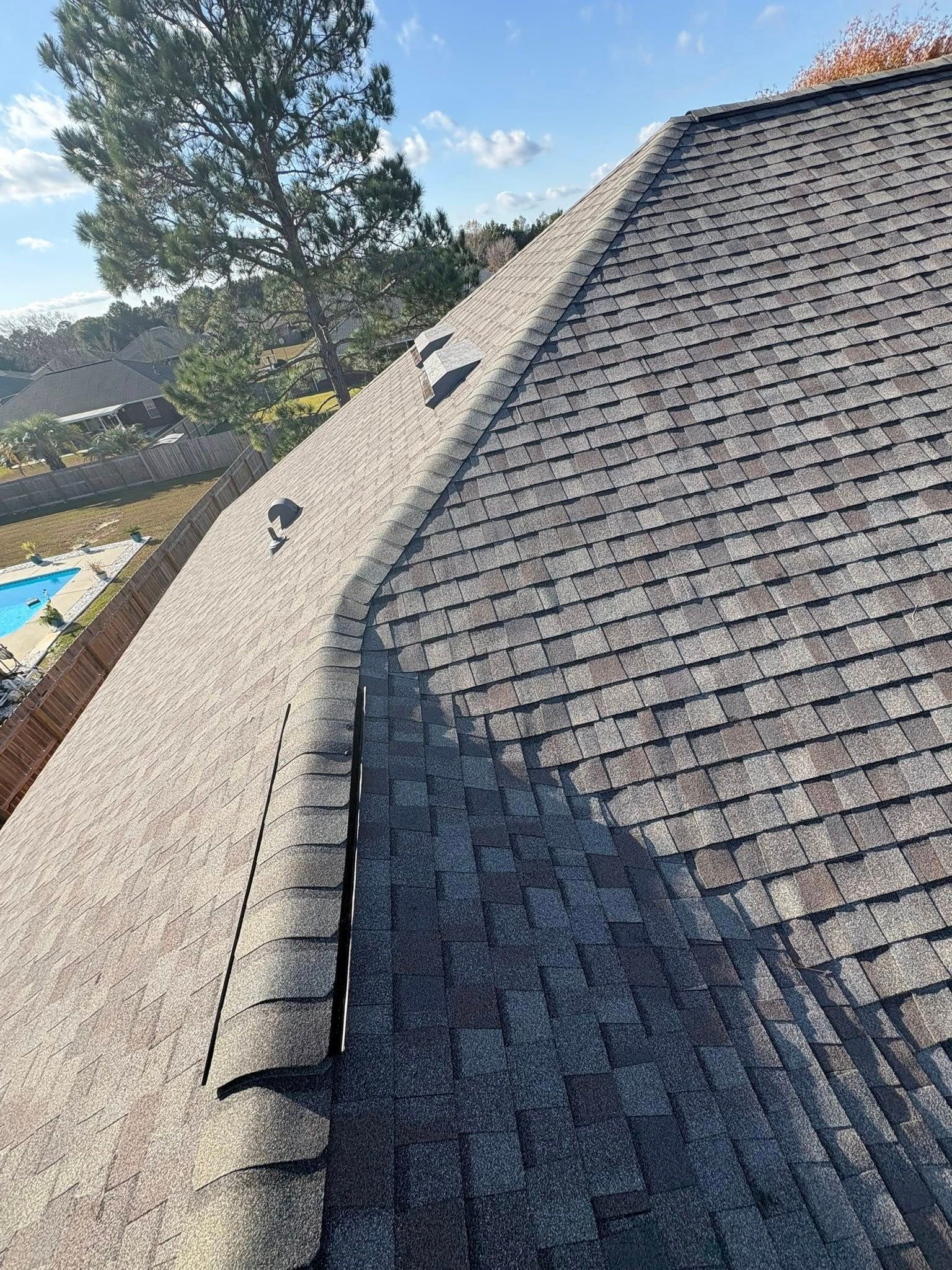 Close-up of a residential asphalt shingle roof, angled view. Brown shingles, vents, clear sky.