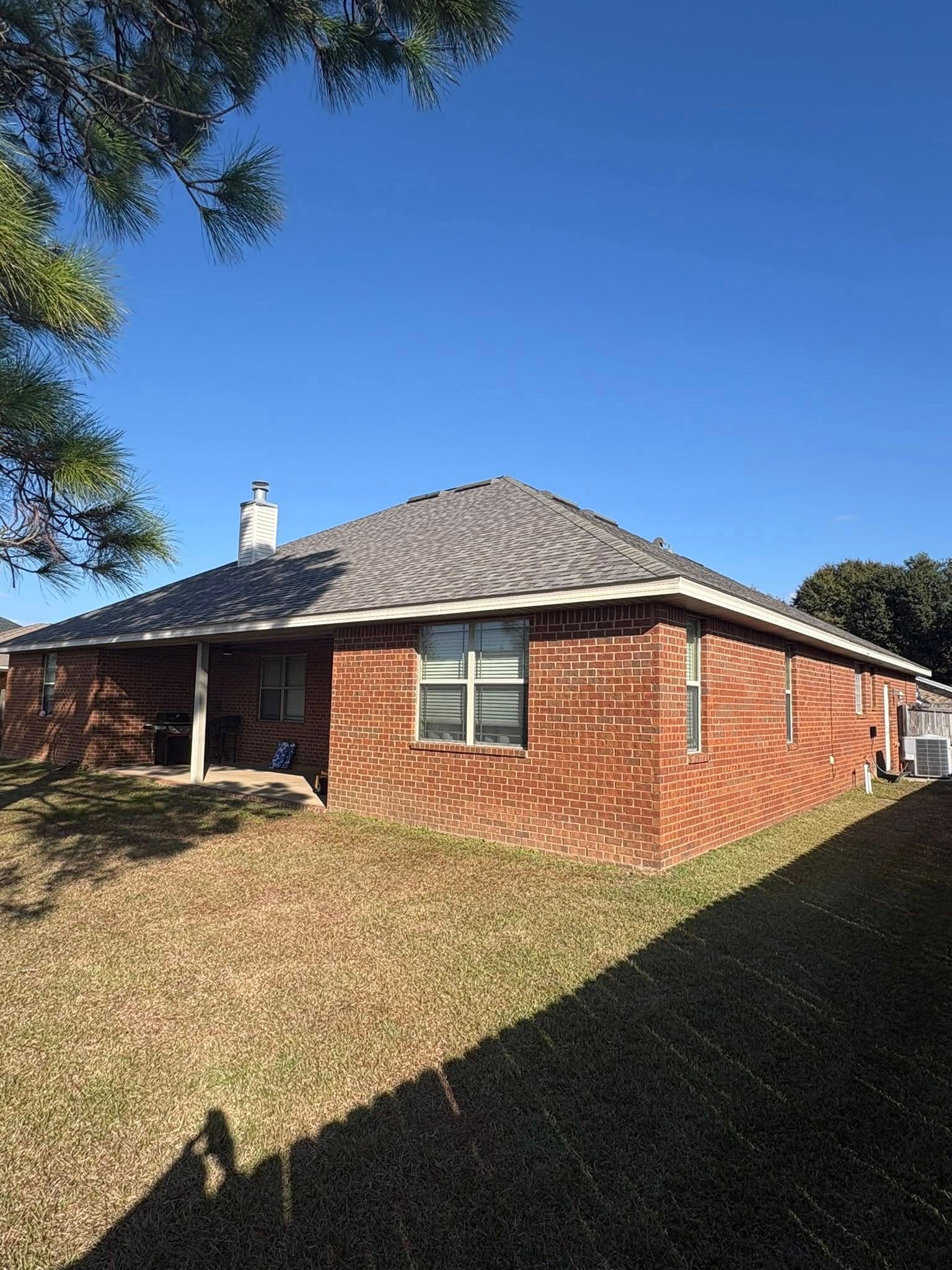 Brick house with gray roof under a clear blue sky; dry, brown grass in the yard.