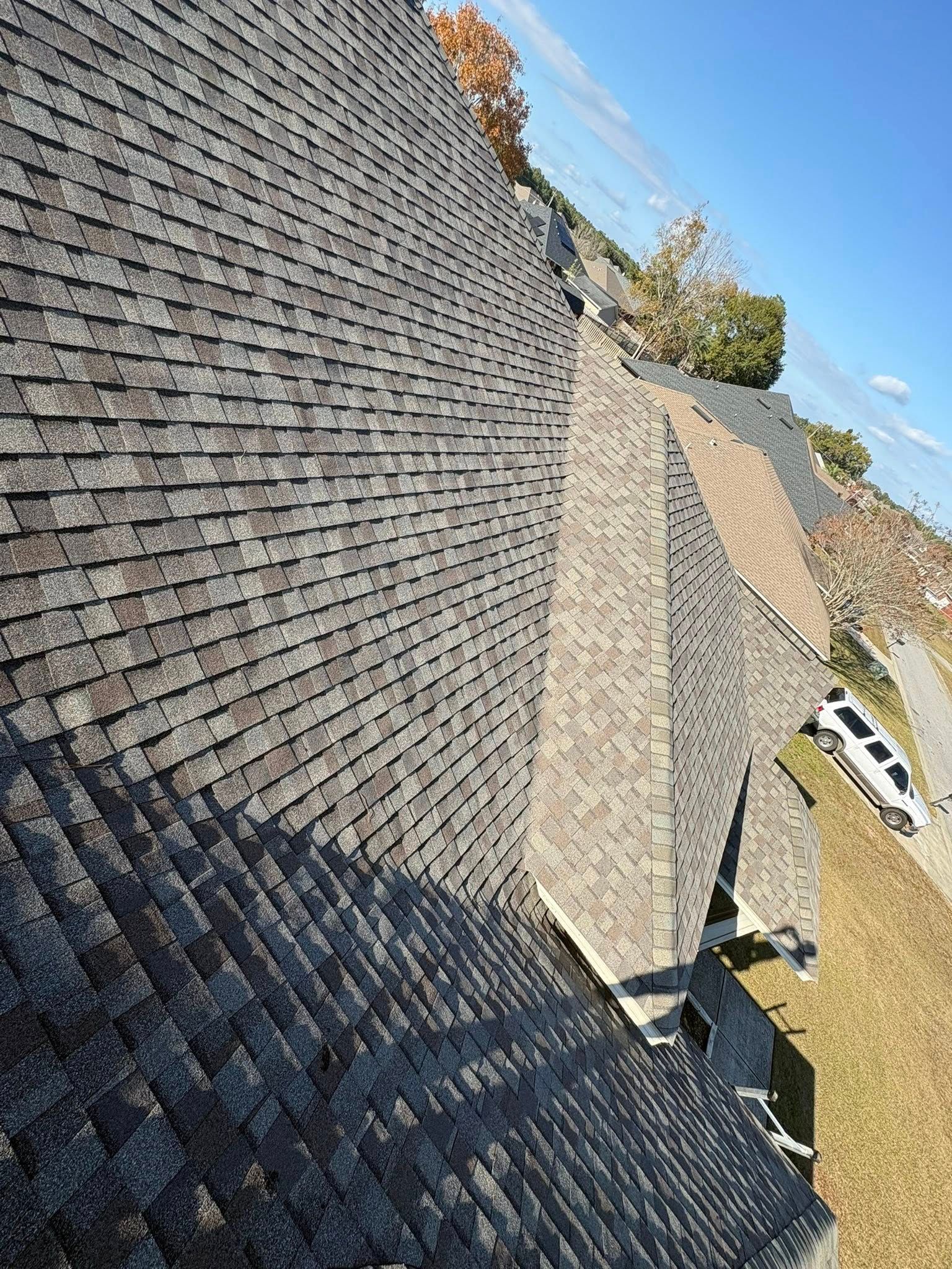 View of a shingled roof with various angles and a blue sky in the background.