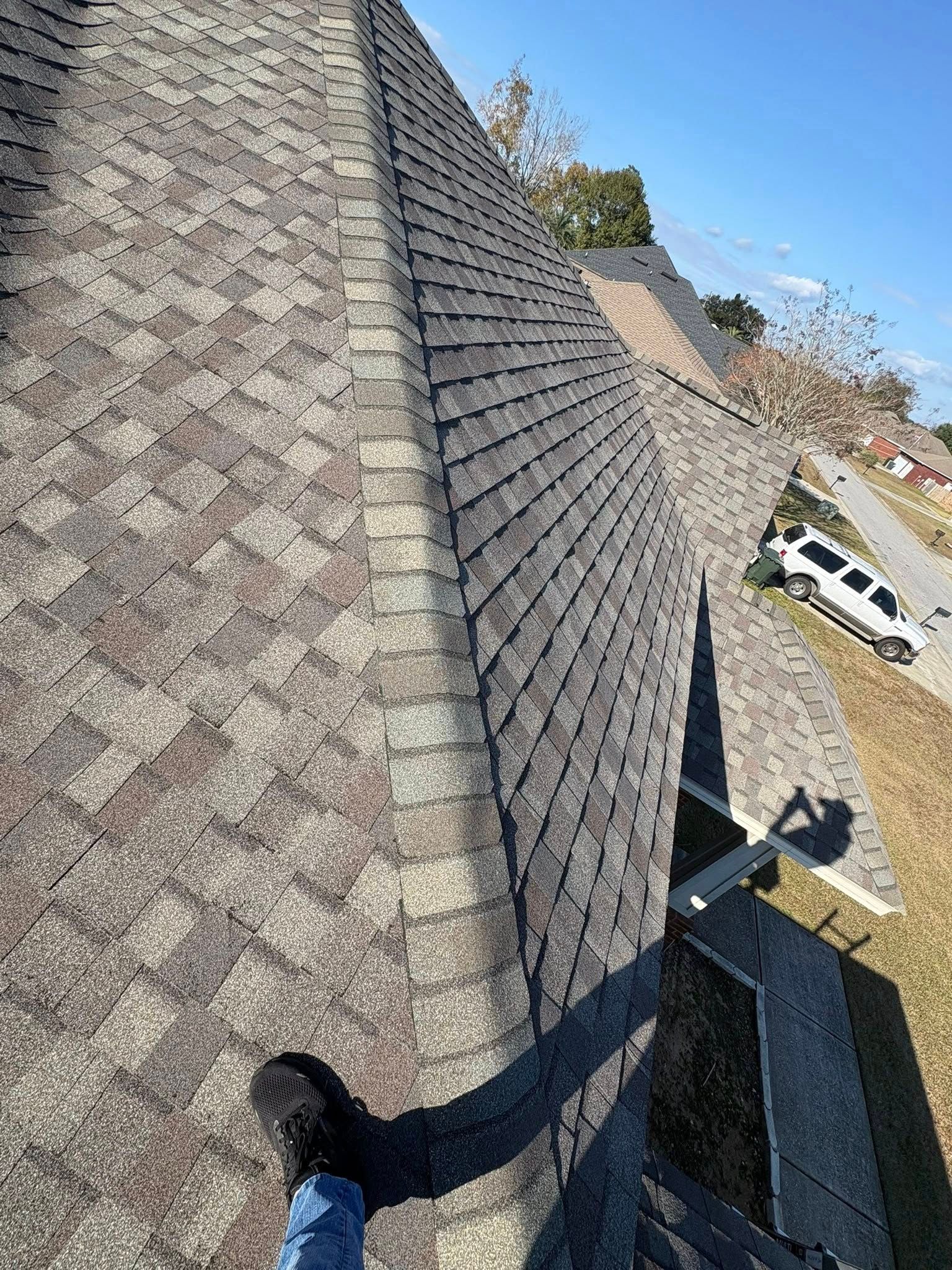 View from a roof, showing shingled surfaces, a shadow, and a foot.