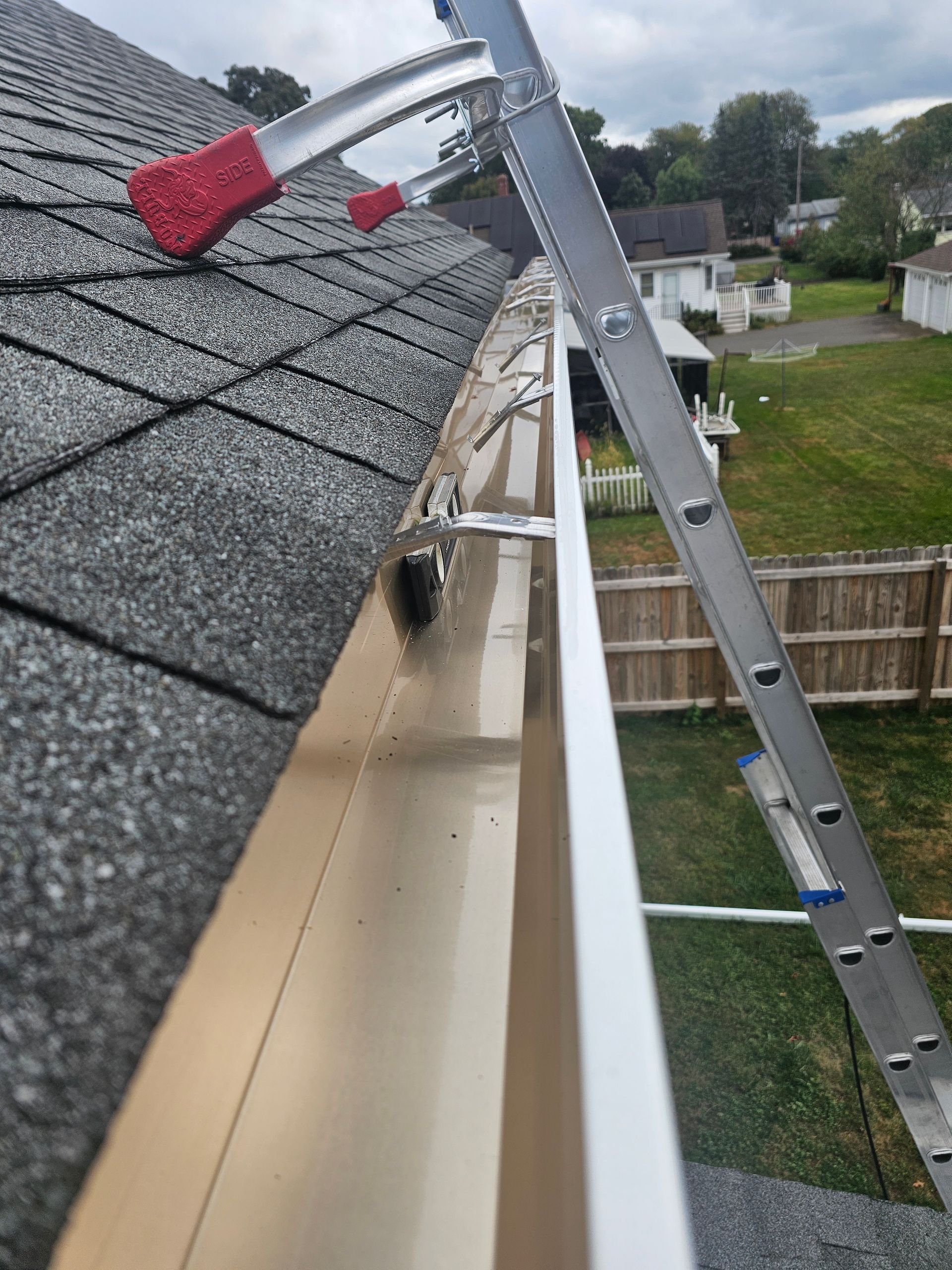 A man wearing a hard hat is fixing a gutter on a roof.
