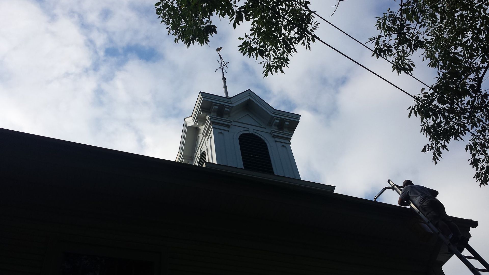 A man on a ladder is working on the roof of a building